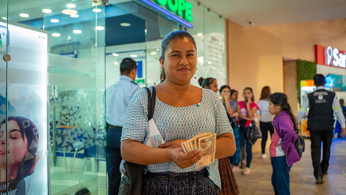 Eine Frau steht dem Eingang einer Bank und hält Bargeld in der Hand