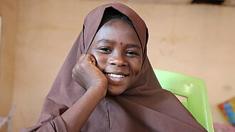 Die 12-jährige Roukaya lächelt in die Kamera. Sie trägt ein braunes Kopftuch.