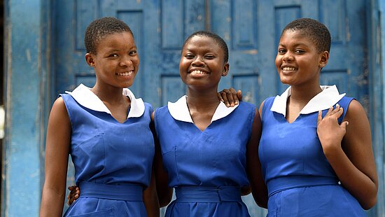 Drei junge Frauen tragen Schuluniformen in blau und lachen in die Kamera.